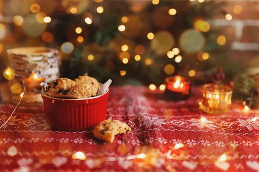 Red festive bowl full with tasty Christmas chocolate cookies, blurred background with Christmas fir tree decorations, lights, garlands and candles. Festive mood at home. High quality photo