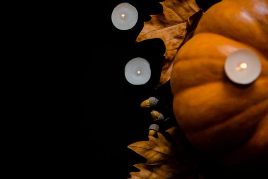 An orange pumpkin with leaves, acorns and candles on a black background. High quality photo