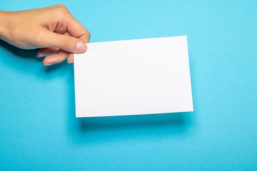 female hand holds a blank piece of paper with copy space in front of a light blue background cardboard