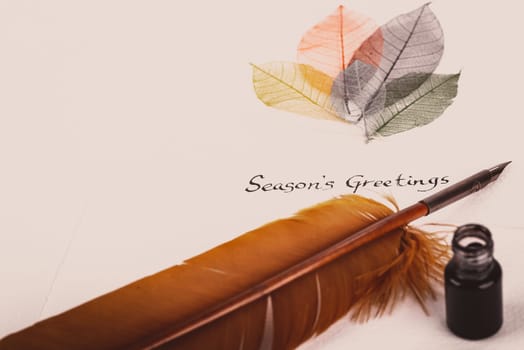 Handwritten Season's Greetings text on rough grain paper, quill pen and inkwell with vintage effect