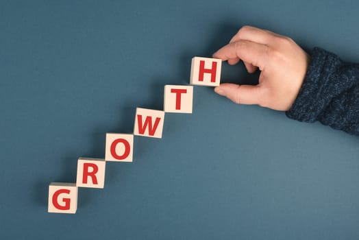 The word growth is standing on wooden cubes,hand is putting the last letter to the row, blue colored background