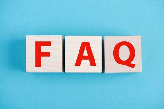 The letters FAQ are standing on wooden cubes, blue colored background, frequently asked questions