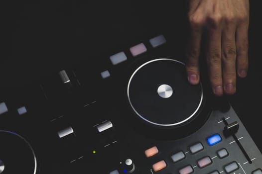 DJ plays music. sound mixer controller with knobs and sliders close up. hands on the mixing deck with turntables at dark with illuminated controls