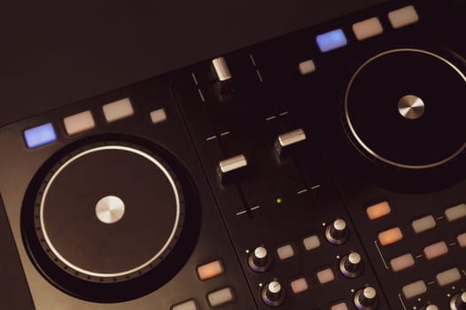 Dj sound mixer controller with knobs and sliders close up. audio mixing deck with turntables at dark with illuminated controls