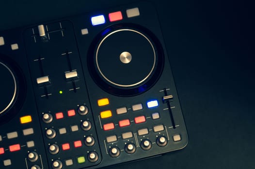 Dj sound mixer controller with knobs and sliders close up. audio mixing deck with turntables at dark with illuminated controls