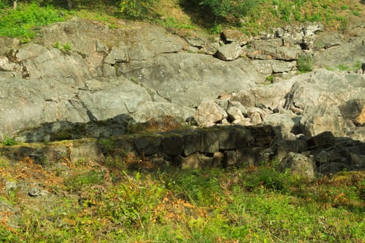 Rock of layered stone overgrown with grass and moss. texture of stone rocks. stone background