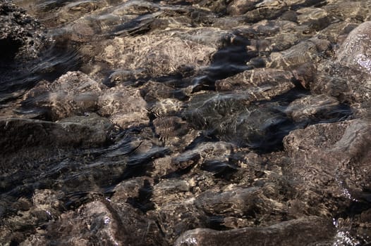 Shiny transparent water. clear water with pebbles and stone on the bottom. shining reflections of sun rays and ripples on the water surface