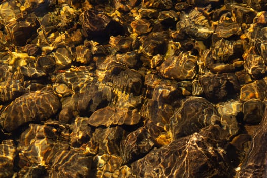Shiny transparent water. clear water with pebbles and stone on the bottom. shining reflections of sun rays and ripples on the water surface