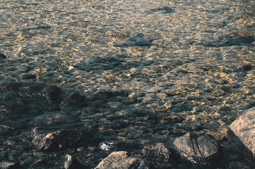 Shiny transparent water. clear water with pebbles and stone on the bottom. shining reflections of sun rays and ripples on the water surface