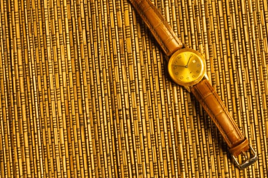Vintage golden wristwatch with leather strap on the bamboo background. copy space