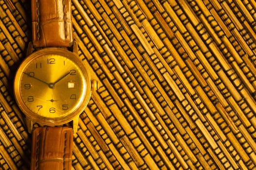 Vintage golden wristwatch with leather strap on the bamboo background. copy space