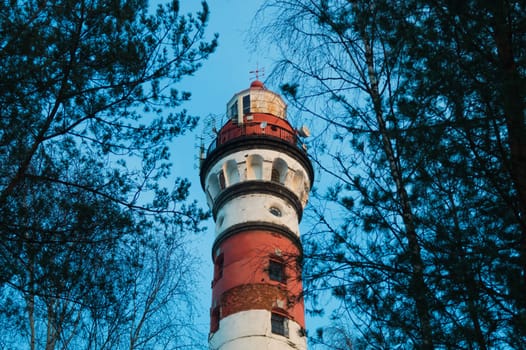 Lighthouse in the forest between the trees. red and white lighthouse background