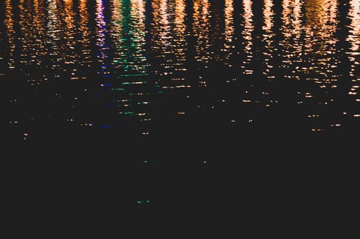 Blurred colorful lights reflect on water surface with ripples in the dark night. abstract background