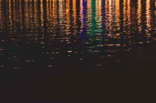 Blurred colorful lights reflect on water surface with ripples in the dark night. abstract background