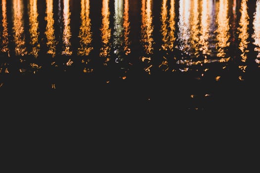 Blurred colorful lights reflect on water surface with ripples in the dark night. abstract background