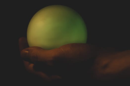 Hand holds a luminous sphere in the dark