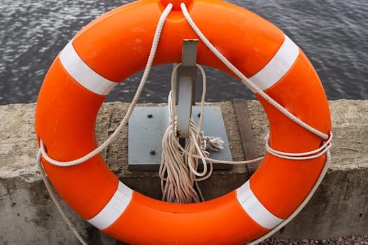 Orange lifebuoy with rope hanging on a pier near the water
