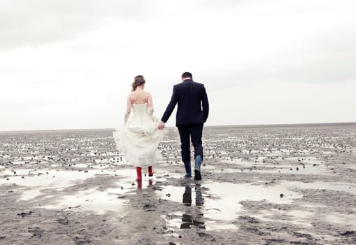 Bride and groom walk in rubber boots in the Wadden Sea