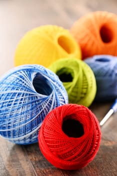 Colorful yarn for crocheting and hook on wooden table