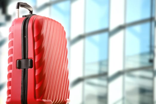 Red plastic travel suitcase in the airport hall.