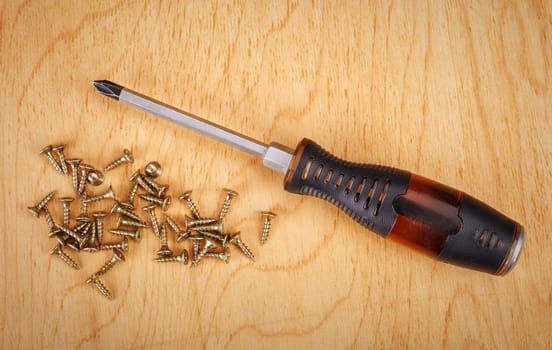 Screws and screwdriver on wooden background.
