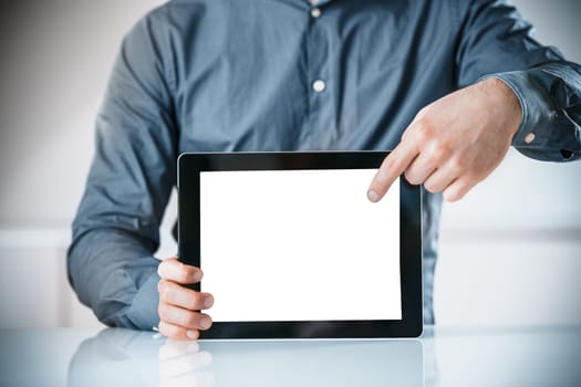 Businessman pointing to a blank white screen on a tablet computer which he is holding balanced on his desk drawing your attention to the empty copyspace, close up view of his hands