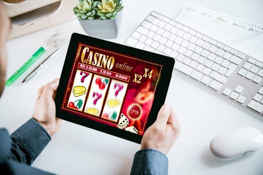 Online casino gambling interface on a tablet showing lucky numbers 777 out of sequence held by a businessman in his office in a gambling addiction concept