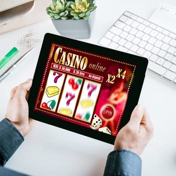 Online gambling concept with a businessman seated at his desk holding a tablet computer showing a casino interface with lucky numbers