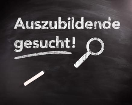 Conceptual Auszubildende Gesucht Phrase on Black Chalkboard with Chalk Stick on Top, Captured in Close up.