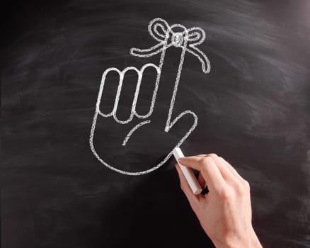 Close up Conceptual Hand with Ribbon on Index Finger Drawing on Black Chalkboard.