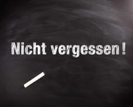 Conceptual Nicht Vergessen or Do not Forget Phrase in White on Black Chalkboard with Chalk on Top.