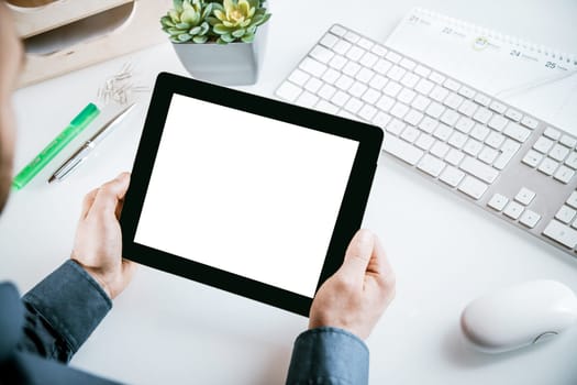 Businessman sitting at his desk at his workstation holding a blank tablet pc with copyspace for your text, closeup high angle view of his hands and the screen