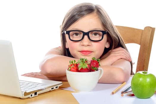 a little girl sitting at his desk with a bowl of strawberries
