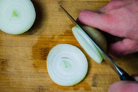 White onion and knife on a wooden cutting board. vegetable slicing process. cooking food