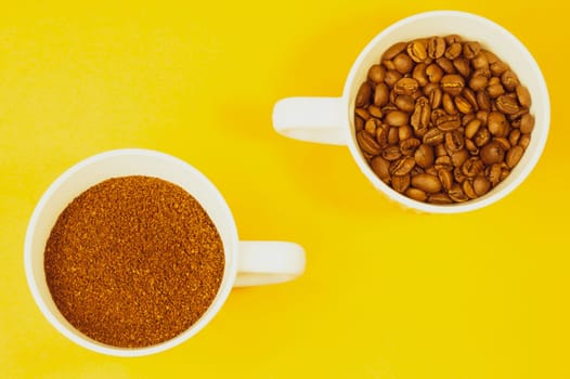 Whole coffee beans and ground coffee in cups on yellow background