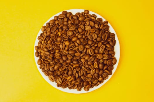 Brown coffee beans on a plate. pile of whole coffee beans on yellow background. copy space