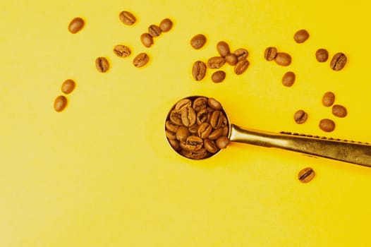 Spoon with roasted coffee beans on yellow background
