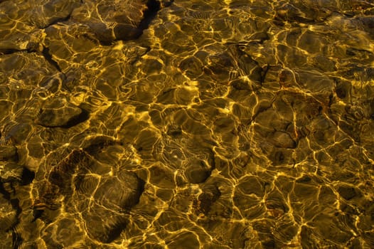 Shiny transparent water. clear water with pebbles and stone on the bottom. shining reflections of sun rays and ripples on the water surface
