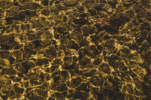 Shiny transparent water. clear water with pebbles and stone on the bottom. shining reflections of sun rays and ripples on the water surface
