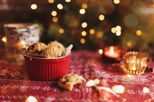 Red festive bowl full with tasty Christmas chocolate cookies, blurred background with Christmas fir tree decorations, lights, garlands and candles. Festive mood at home. High quality photo