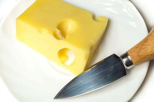 Cheese with a cheese knife on a white plate. piece of cheese with holes