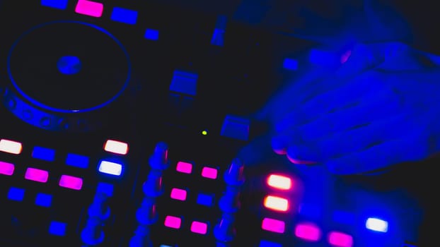 DJ plays music. sound mixer controller with knobs and sliders close up. hands on the mixing deck with turntables at dark with illuminated controls