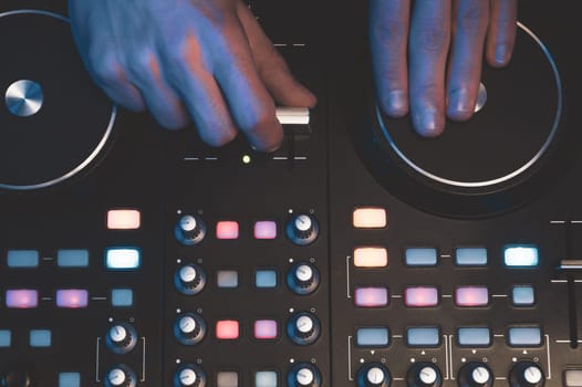 DJ plays music. sound mixer controller with knobs and sliders close up. hands on the mixing deck with turntables at dark with illuminated controls