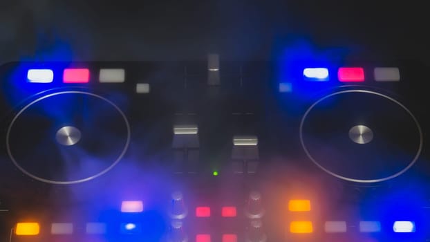 Dj sound mixer controller with knobs and sliders close up. audio mixing deck with turntables at dark with illuminated controls