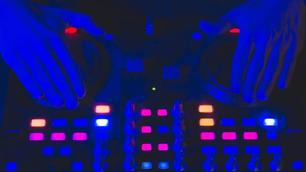 DJ plays music. sound mixer controller with knobs and sliders close up. hands on the mixing deck with turntables at dark with illuminated controls