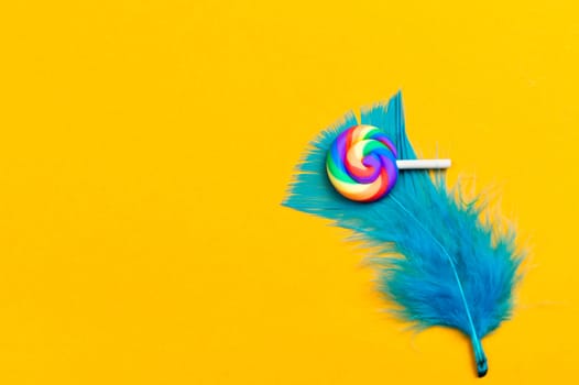 Lollipop lies on a feather. spiral candy on a yellow background. holiday decoration. copy space