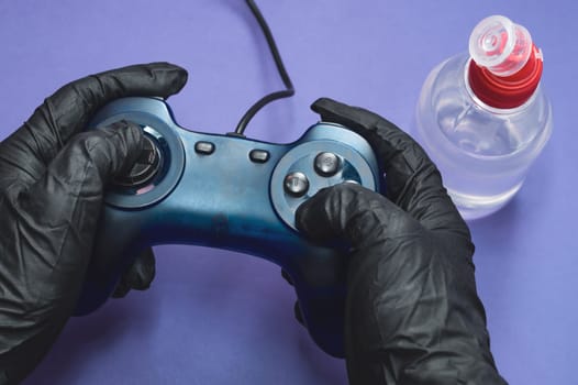 Hands in protective gloves holding the gamepad. play video games. bottle of antiseptic