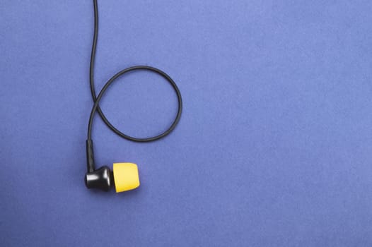 Earphone with yellow ear cushion on a blue background. in-ear headphones. audio equipment. copy space