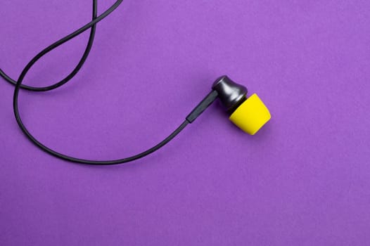 Earphone with yellow ear cushion on a purple background. in-ear headphones. audio equipment