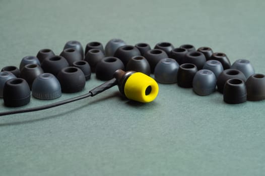 Individuality concept. earphone with yellow ear cushion opposite a row of gray embouchures. in-ear headphones. modern style. audio equipment